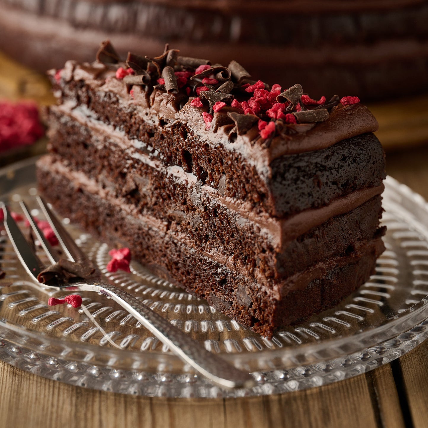 Slice of vegan dark chocolate and raspberry cake showing chocolate sponge, frosting and raspberry jam filling